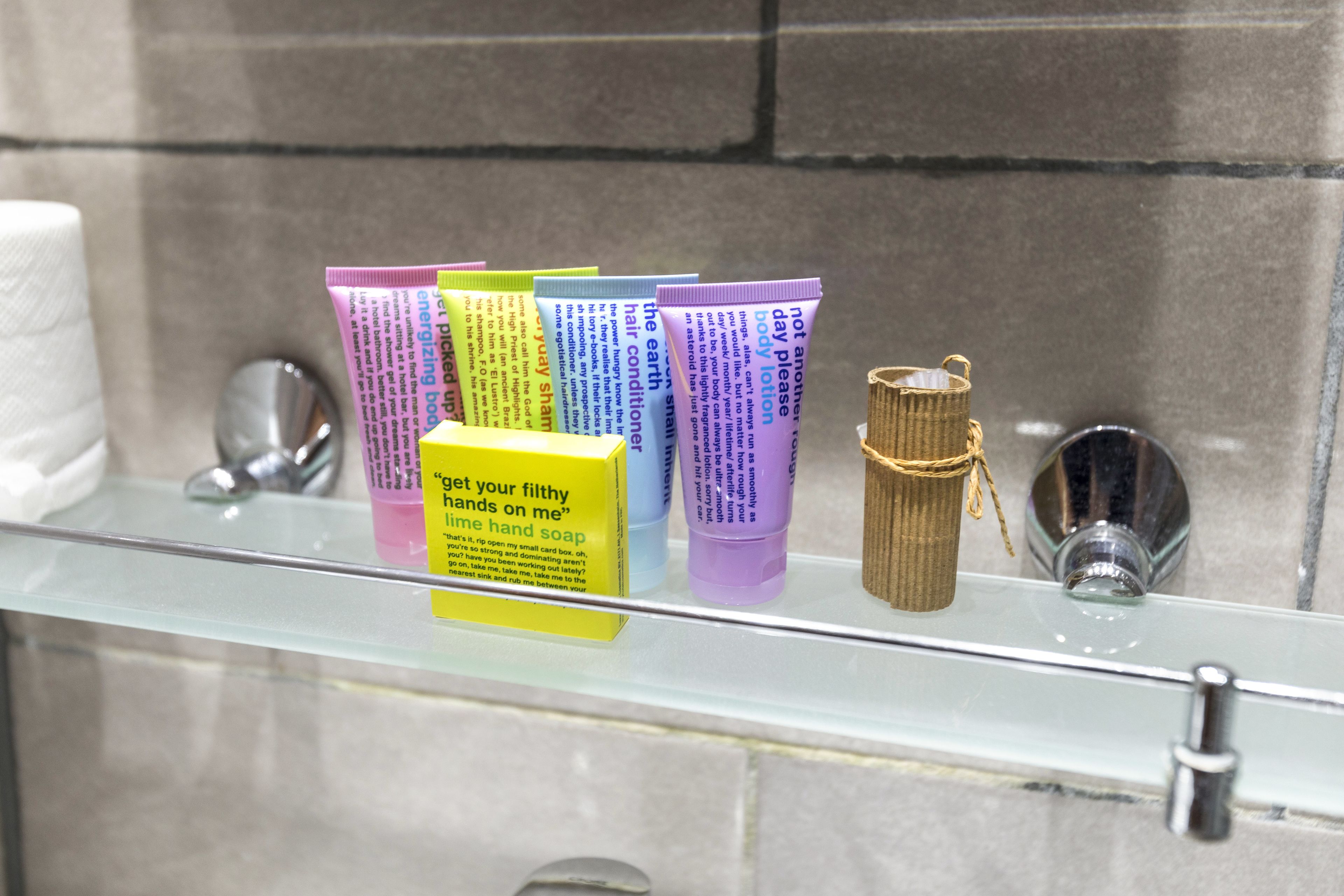 A bathroom shelf with various toiletries including a yellow box, several tubes of hand soap, and a small bottle of lotion.