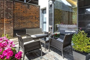 An outdoor patio with wicker furniture, a glass table, and potted plants. - Hotel Shepherds Bush London (London)
