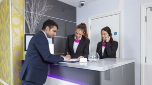 A reception desk with a modern design, a digital screen, and a glass partition. - Hotel Shepherds Bush London (London)