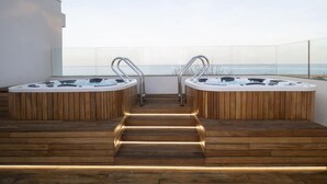 Une terrasse sur le toit dotée de deux bains à remous, d’un escalier en bois et d’une balustrade en verre offrant une vue sur la mer.