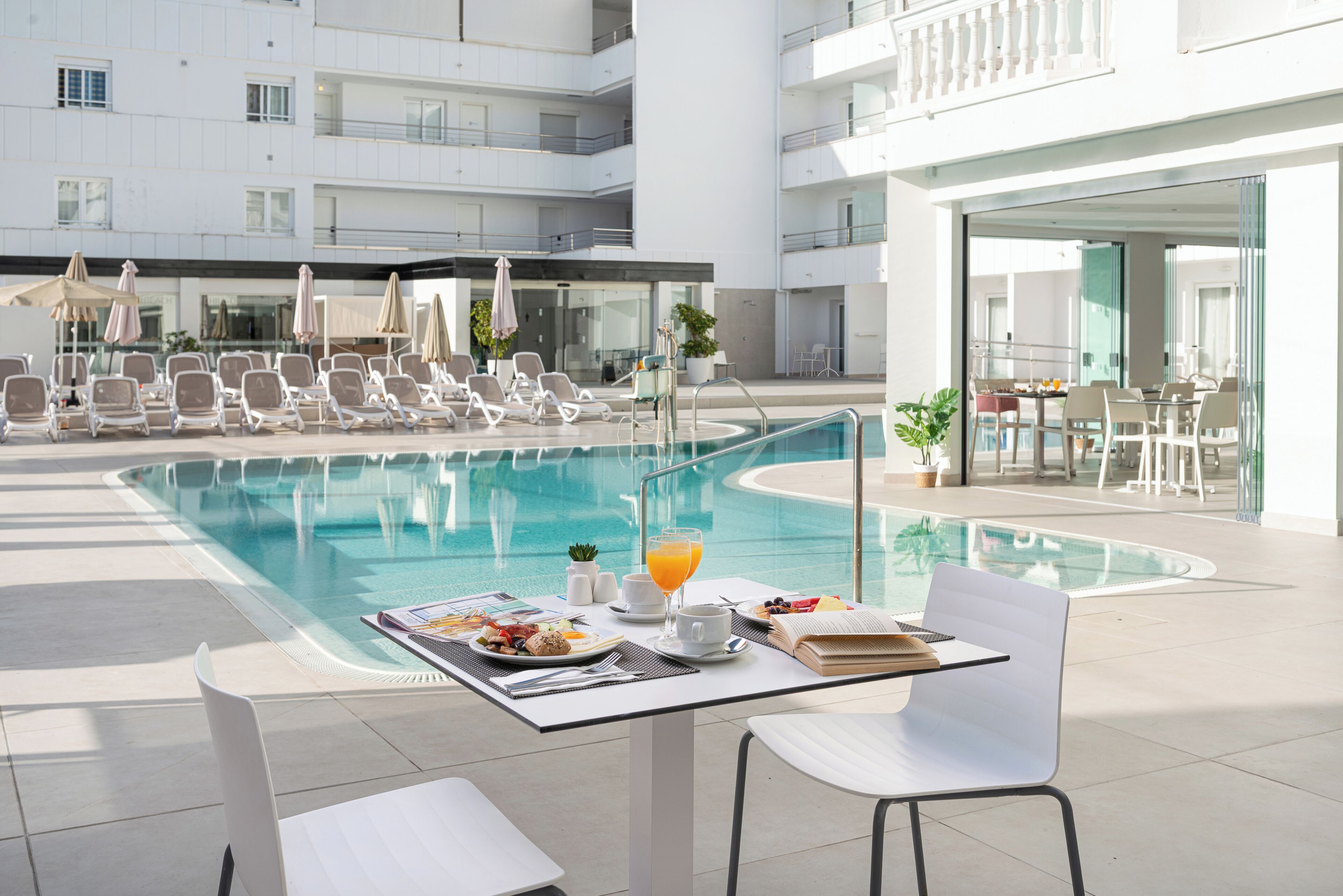 A poolside dining area with a table set for breakfast, lounge chairs, and a view of the pool.