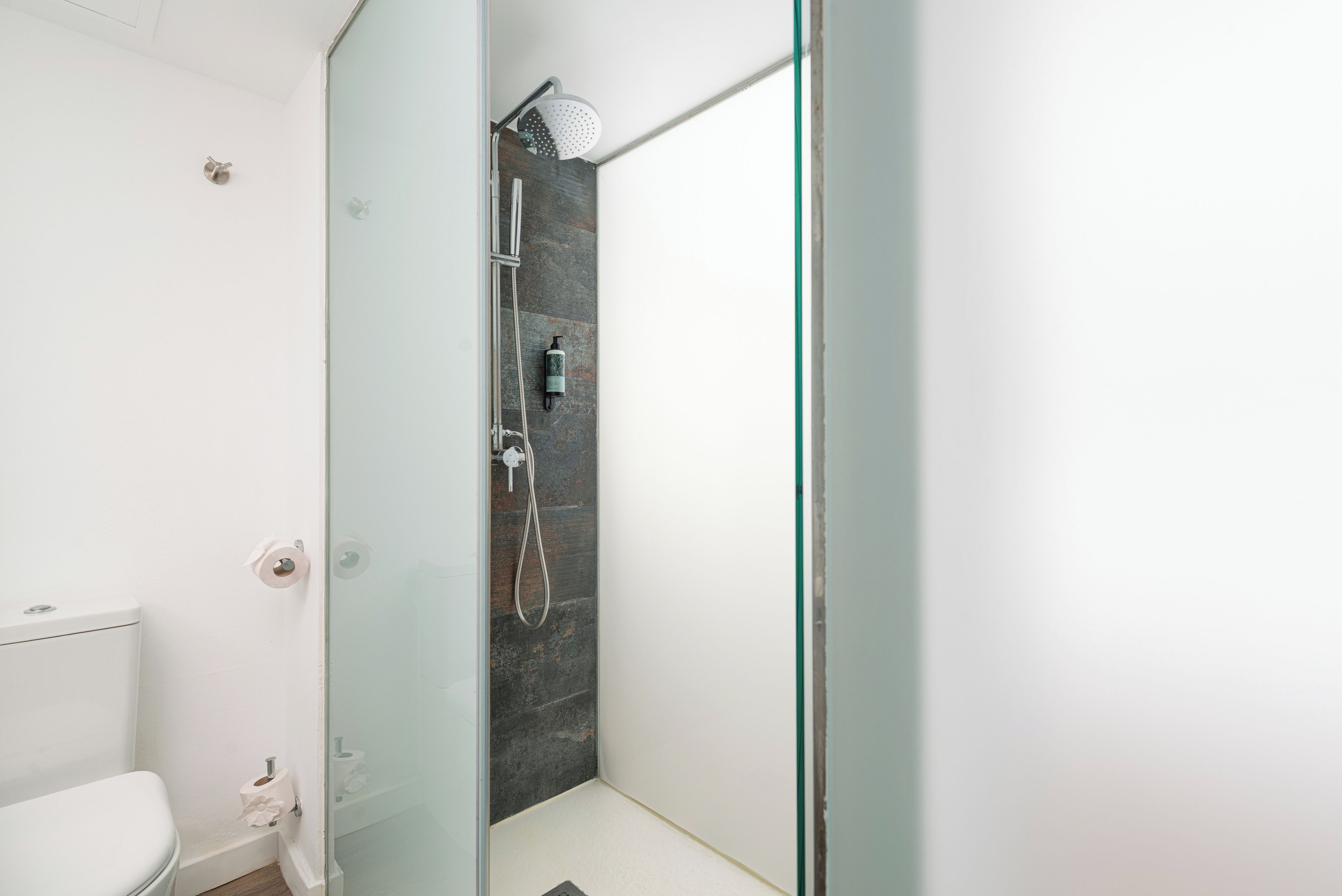 Ein modernes Badezimmer mit Duschkabine aus Glas, Toilette und sichtbarer Dusche.