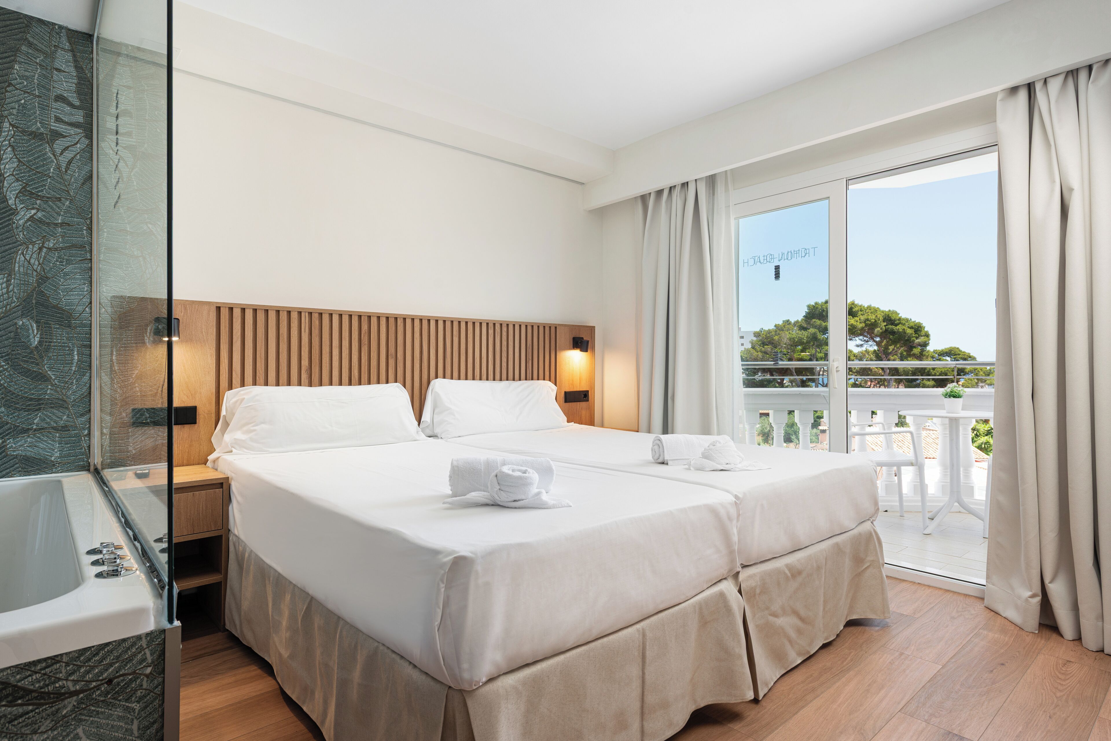 A hotel room with a bed, bedside table, and a glass-enclosed bathroom.