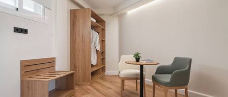 Una habitación moderna y minimalista con un banco de madera, una silla blanca, una mesita con una planta y un armario de madera.