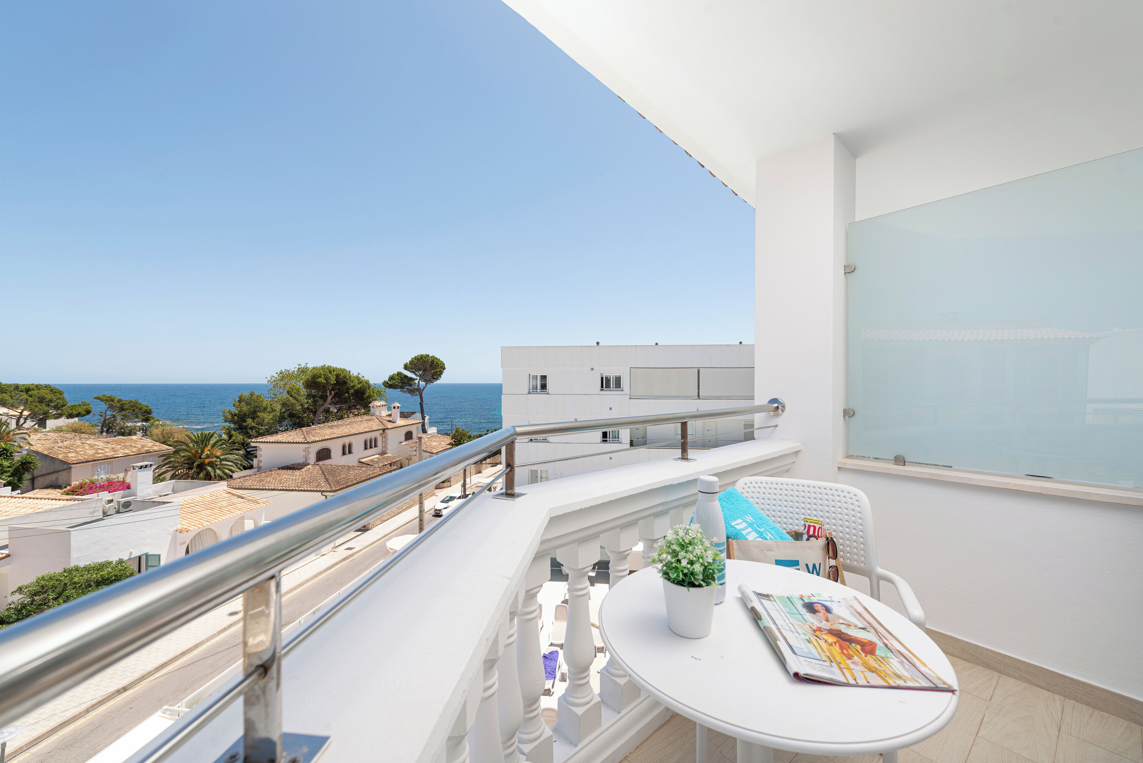 A balcony with a view of the sea, a white table with a magazine, and a potted plant.