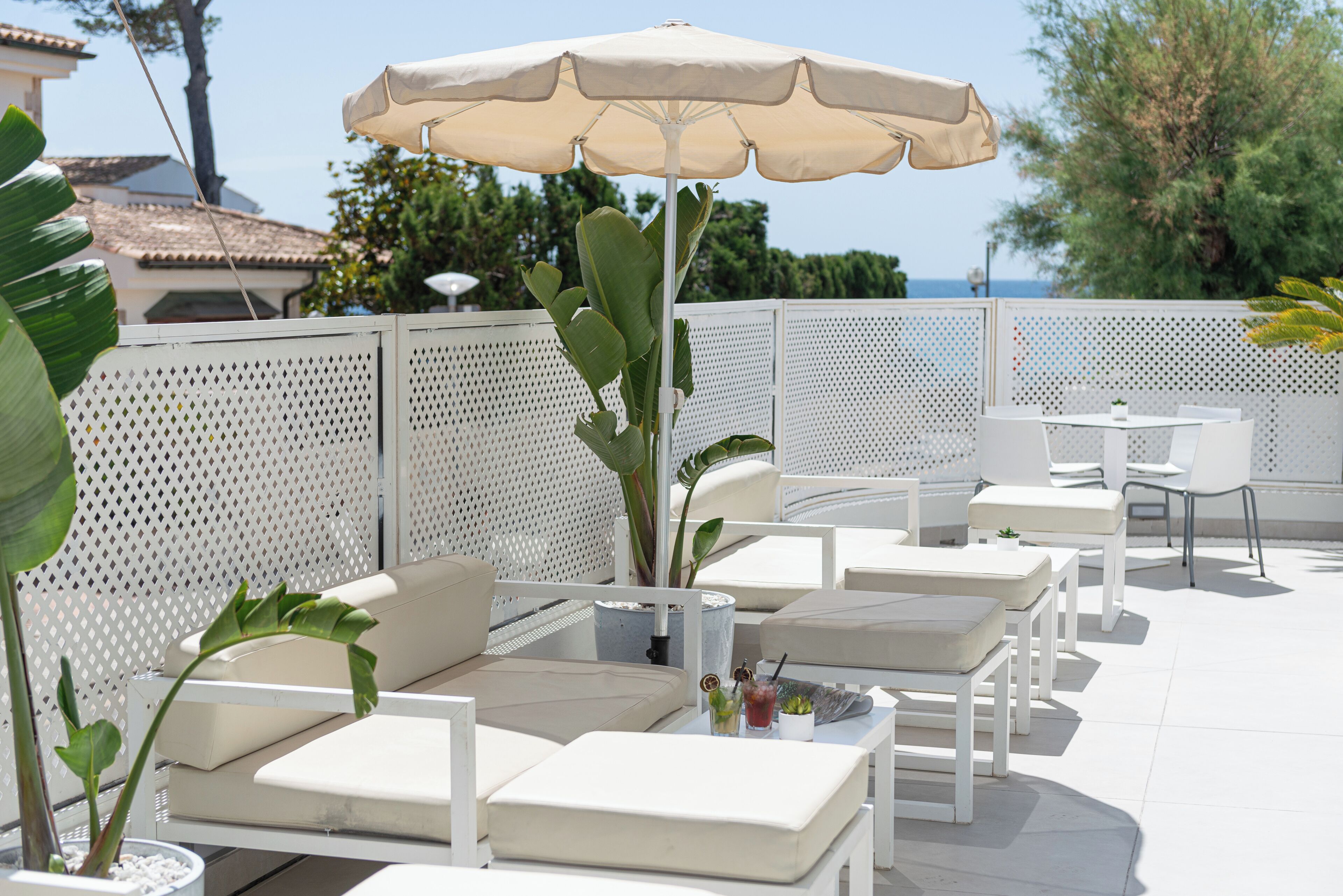 An outdoor seating area with white furniture, a large umbrella, and a view of the sea.