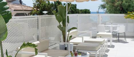 An outdoor seating area with white furniture, a large umbrella, and a view of the sea.
