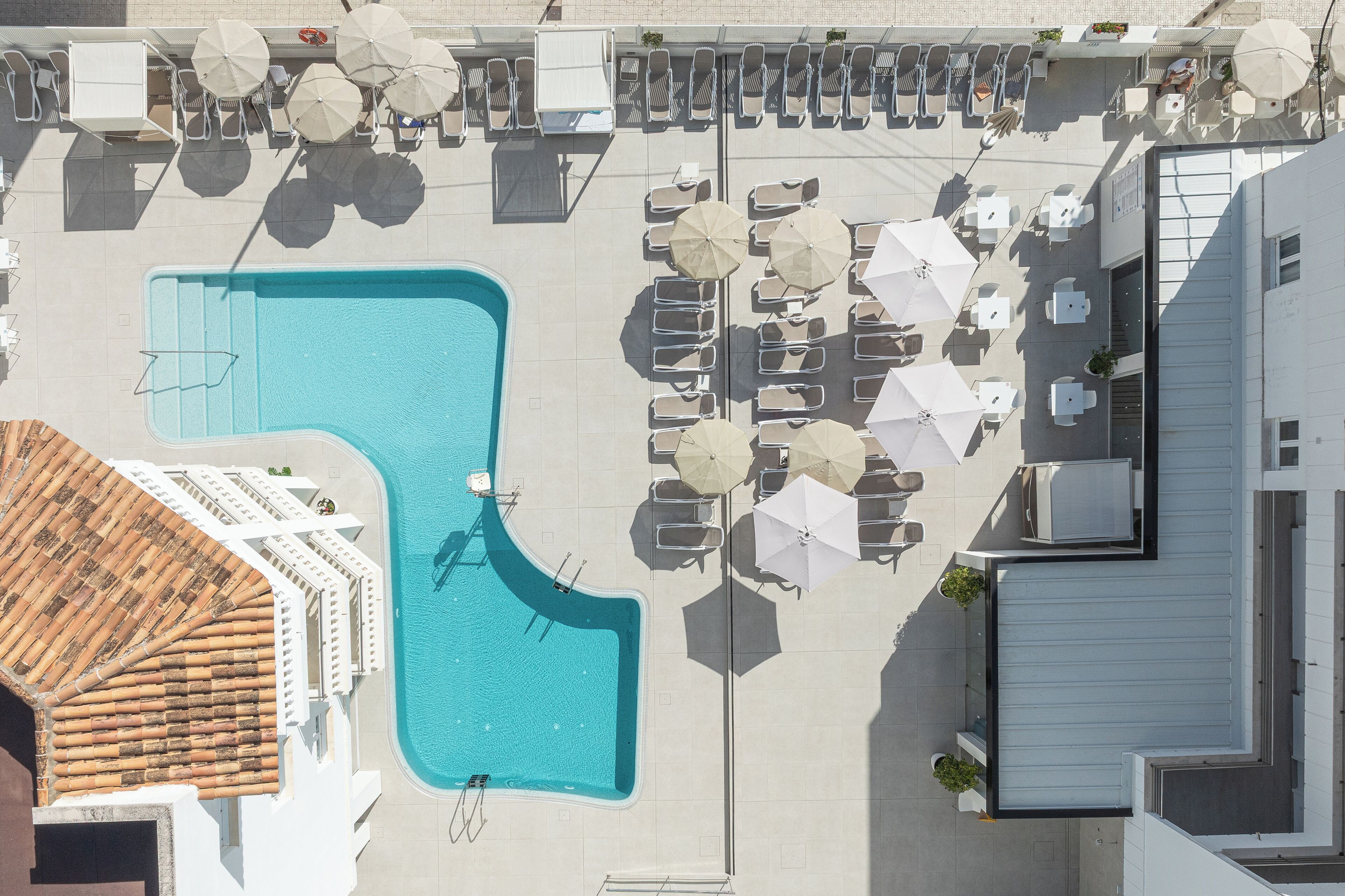 Vista aérea de un hotel con piscina, tumbonas y sombrillas.