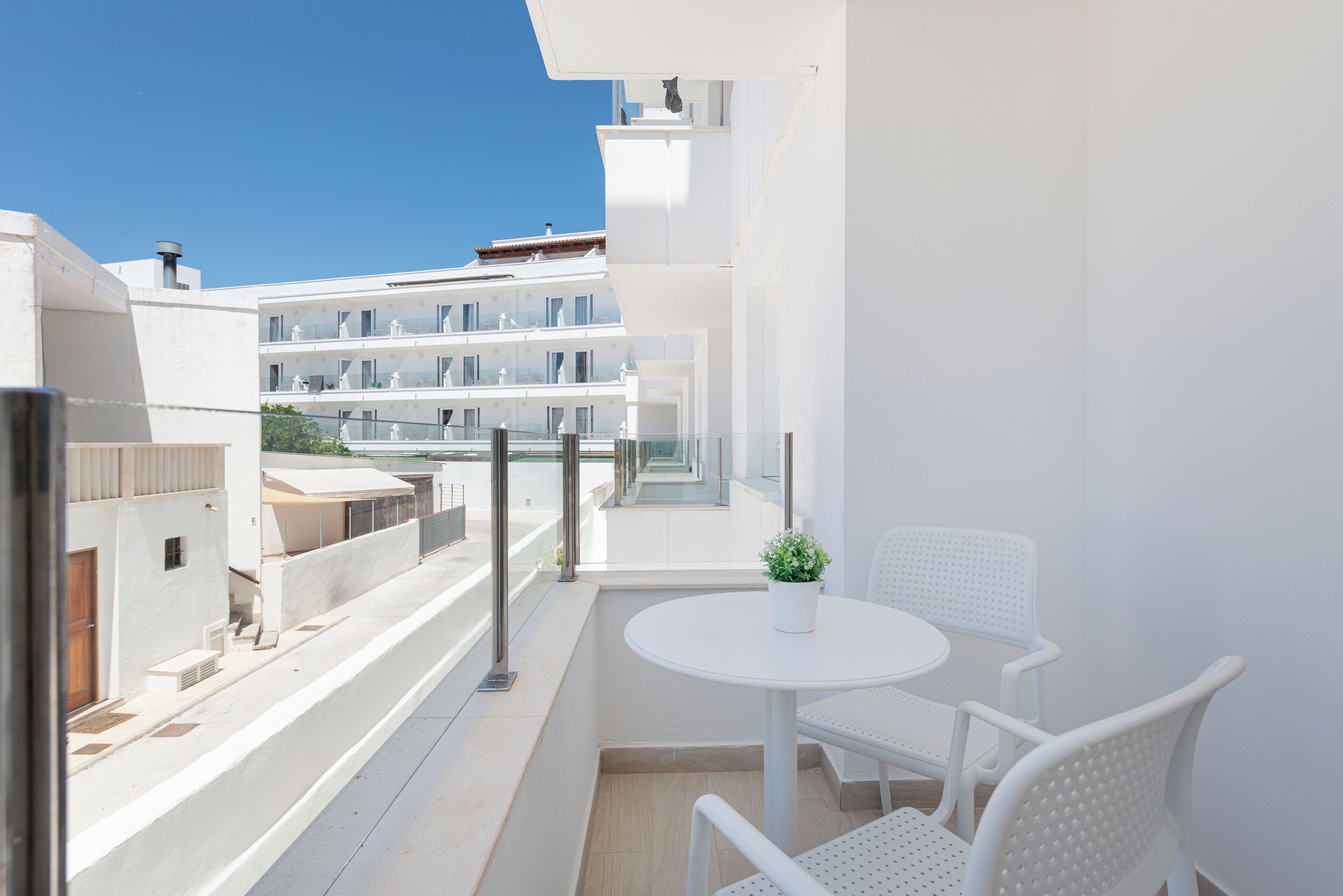 Un balcón con una mesa blanca y dos sillas blancas, con vista a un edificio moderno con varios balcones.