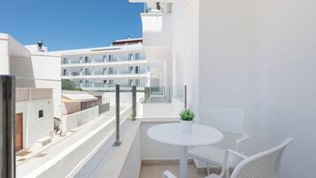 Un balcón con una mesa blanca y dos sillas blancas, con vista a un edificio moderno con varios balcones.
