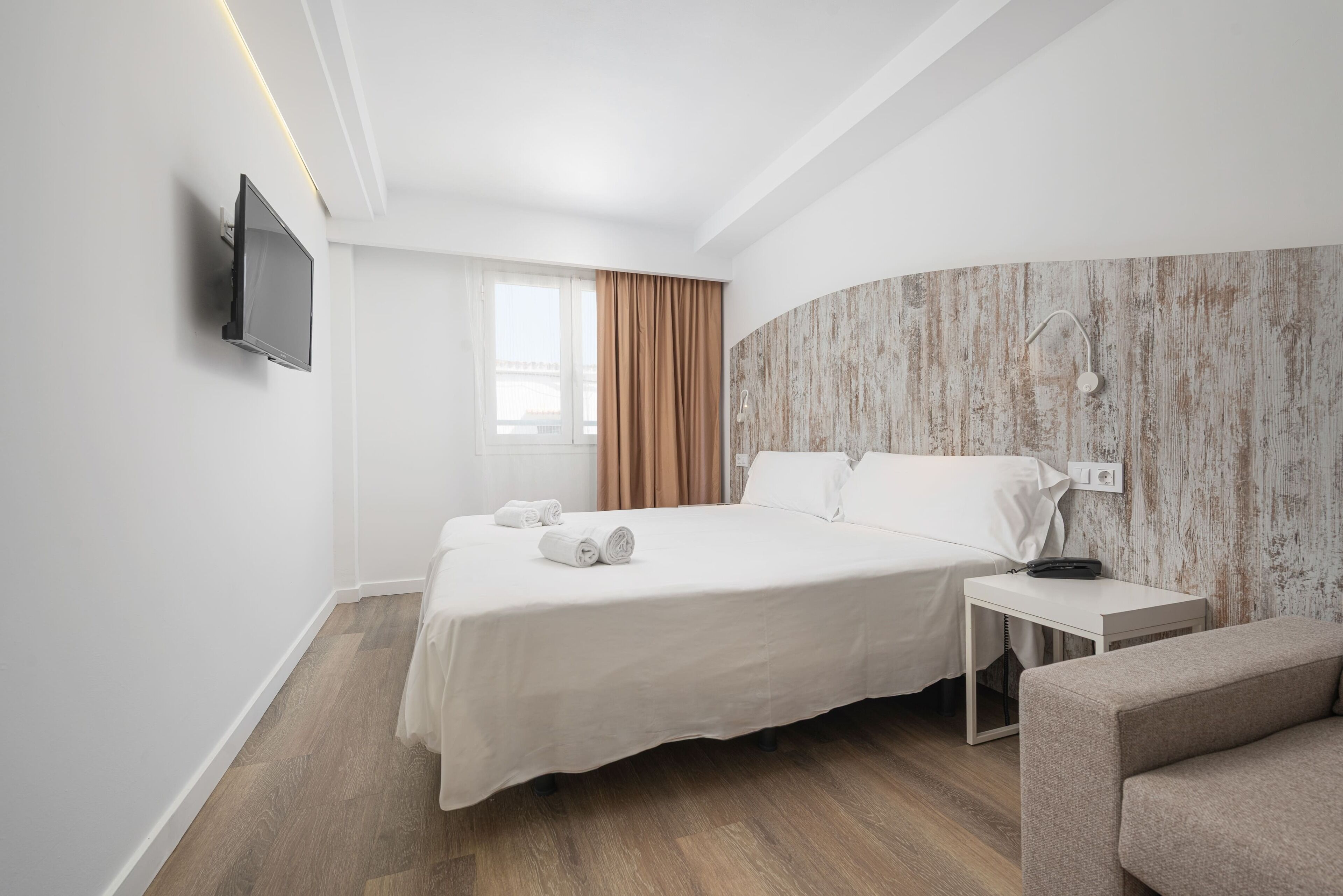 Habitación de hotel con cama, televisión, mesita de noche y zona de ducha.