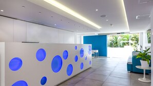 Un área de recepción moderna con un mostrador blanco que presenta patrones circulares azules, una pared de acento azul y vistas al exterior.