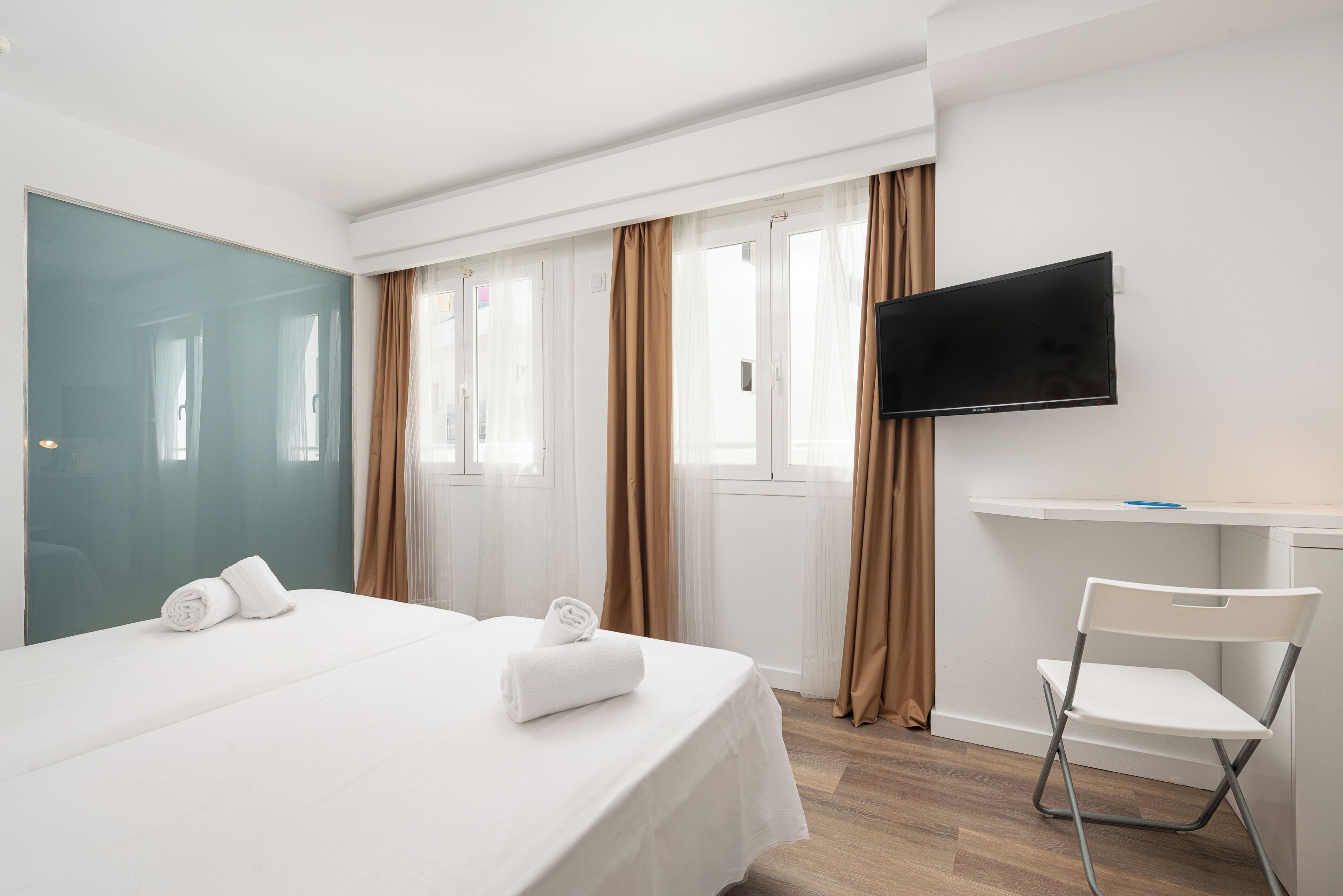Quarto de hotel com cama, televisão, secretária e cadeira.