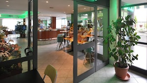 A coffee shop with a neon sign, indoor seating, and a large potted plant. - Hotel delle Alpi (Turin)