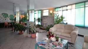 A spacious living room with a beige sofa, a coffee table with magazines, and several potted plants. - Hotel delle Alpi (Turin)