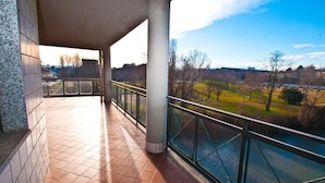 A covered outdoor area with tiled flooring, a glass railing, and a view of a river and park. - Hotel delle Alpi (Turin)