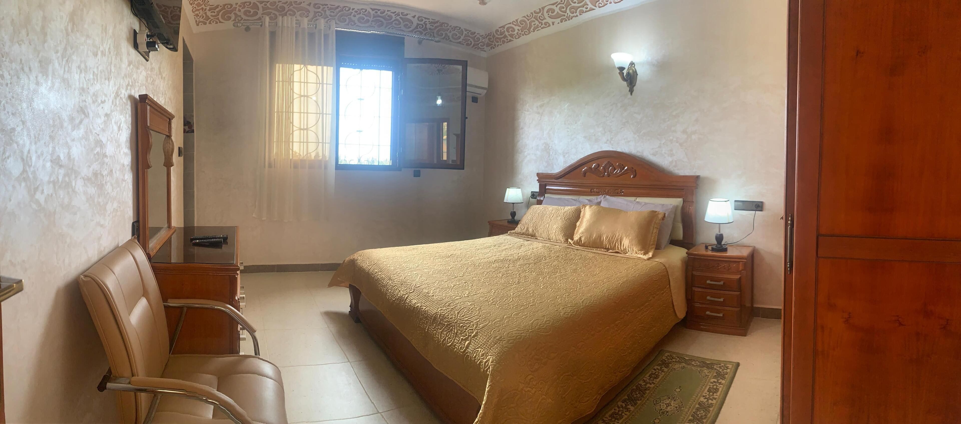 Una habitación de hotel con una cama grande, una mesita de noche de madera, un escritorio con una silla, un espejo y un armario.