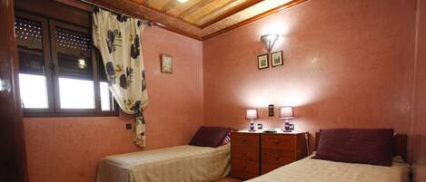 A bedroom with two single beds, a wooden dresser, a nightstand, and a window with curtains.
