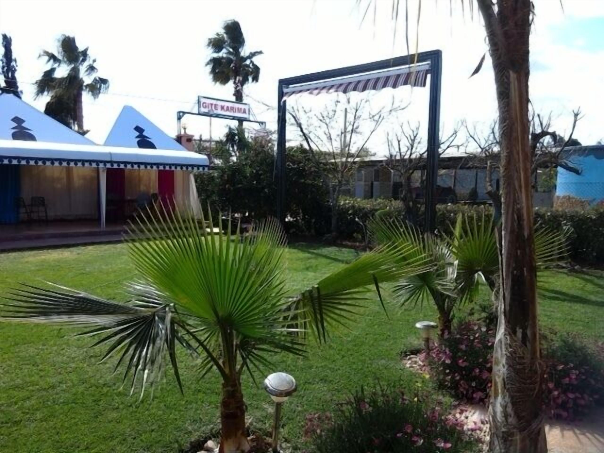 Un jardín con palmeras y un edificio con un letrero que dice "GITE KARIMA".