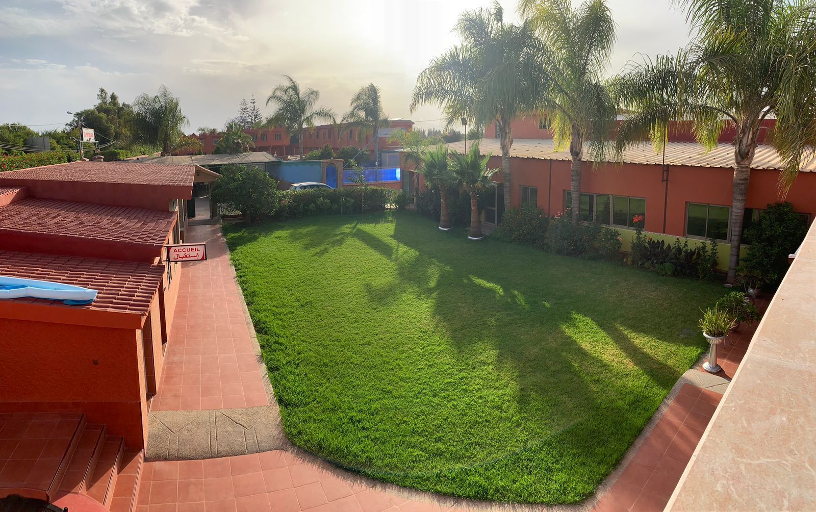 A courtyard with a well-maintained lawn, palm trees, and a building with a red facade.