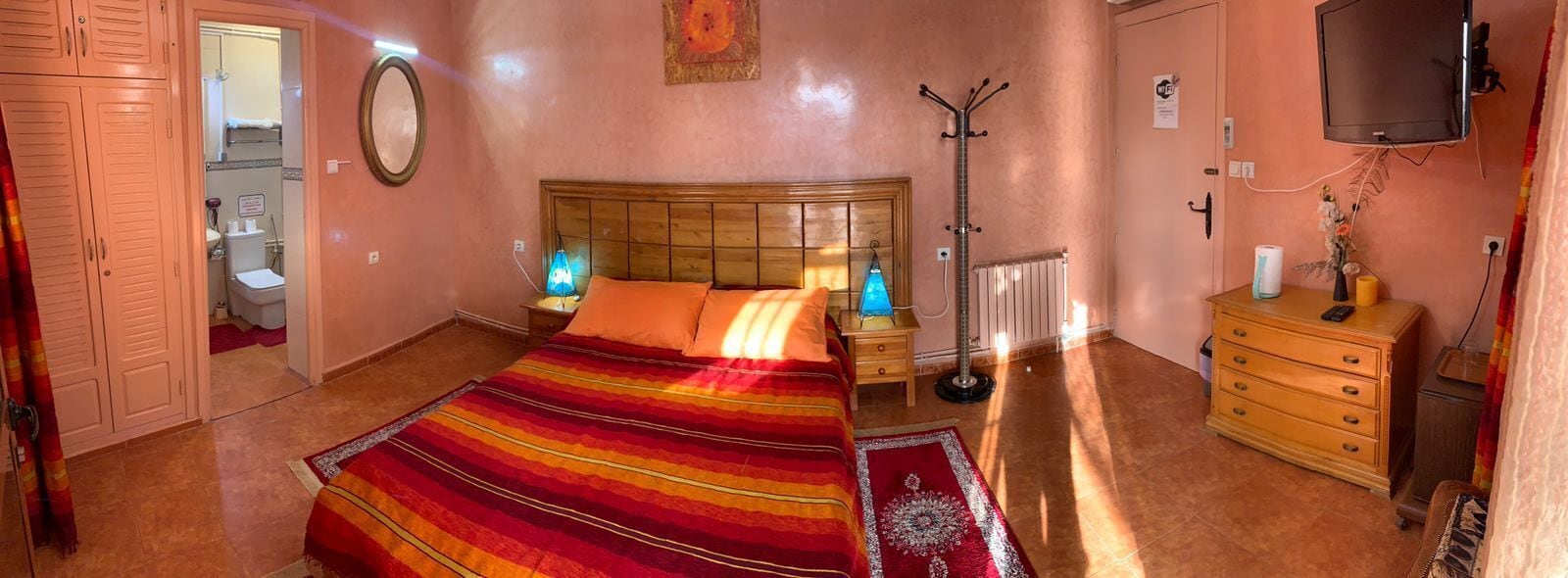 A bedroom with a bed, bedside lamps, a dresser, a radiator, and a television.