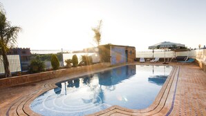 A swimming pool with a tiled deck, a fence, and a building with a mural.