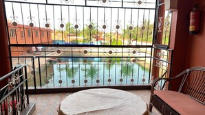 A balcony with a view of a swimming pool, a table, and a chair.