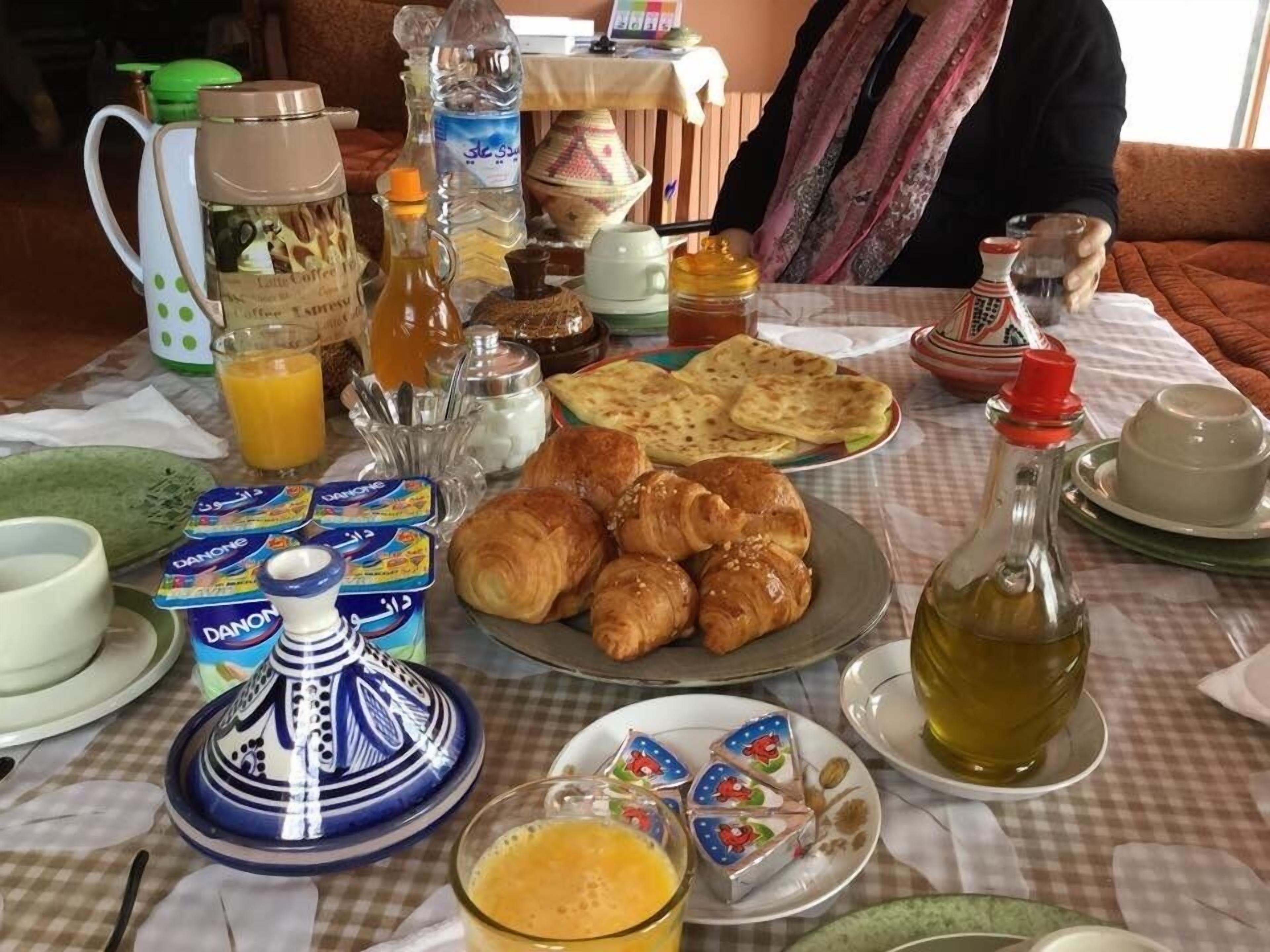 A breakfast table with croissants, juice, Danone yogurt, and various condiments.