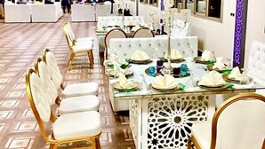 A banquet hall with a long table set for a formal event, surrounded by white upholstered chairs with gold accents.