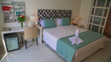 A hotel room with a bed, a desk, a chair, a refrigerator, and a wall with a geometric pattern.