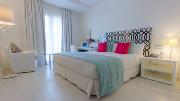 A modern hotel room with a large bed, a desk, a chair, and a nightstand.
