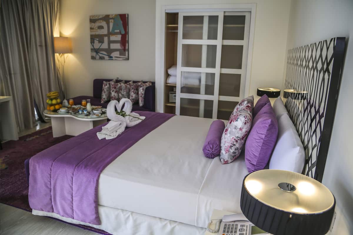 Habitación de hotel con cama, mesita de noche con lámpara, armario y un cuadro en la pared.