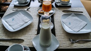 A breakfast table set with plates, bowls, a teapot, and a cup of orange juice. - Hôtel al Mandari (Tetouan)