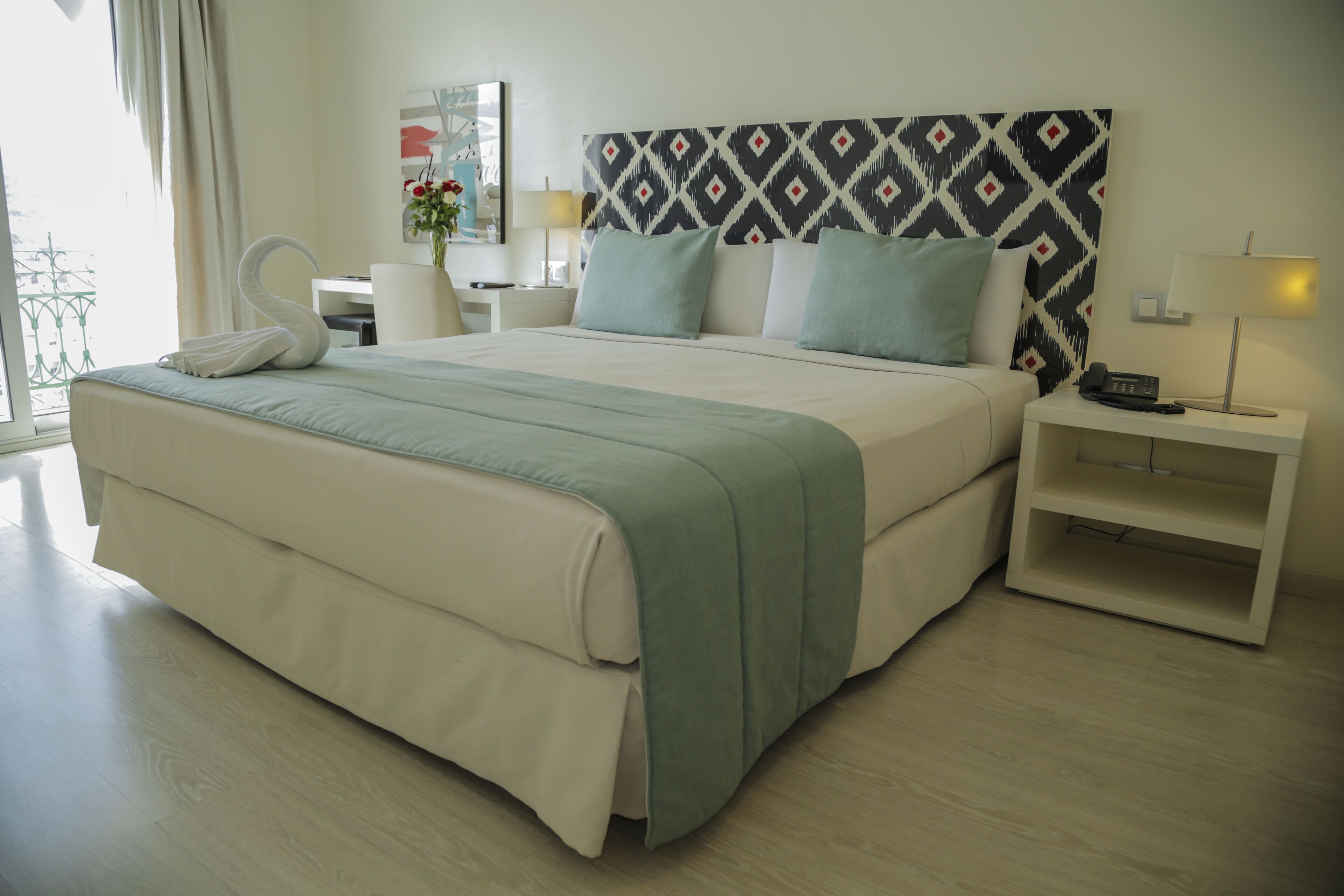 A hotel room with a large bed, a nightstand, a desk, and a chair.