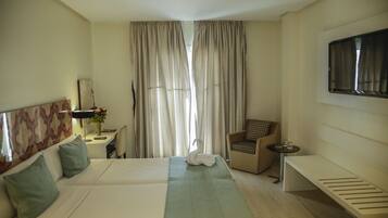 Habitación de hotel con una cama grande, un escritorio con lámpara, una silla, un banco y un televisor montado en la pared.