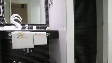 Un baño con suelo de baldosas negras, cabina de ducha de cristal, lavabo blanco con espejo y dos toallas colgadas en la pared.