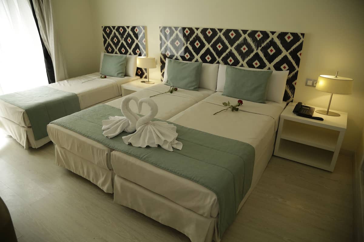 Habitación de hotel con dos camas, una cama grande con un cisne decorativo en la colcha y una cama más pequeña. Hay mesitas de noche con lámparas y un teléfono.
