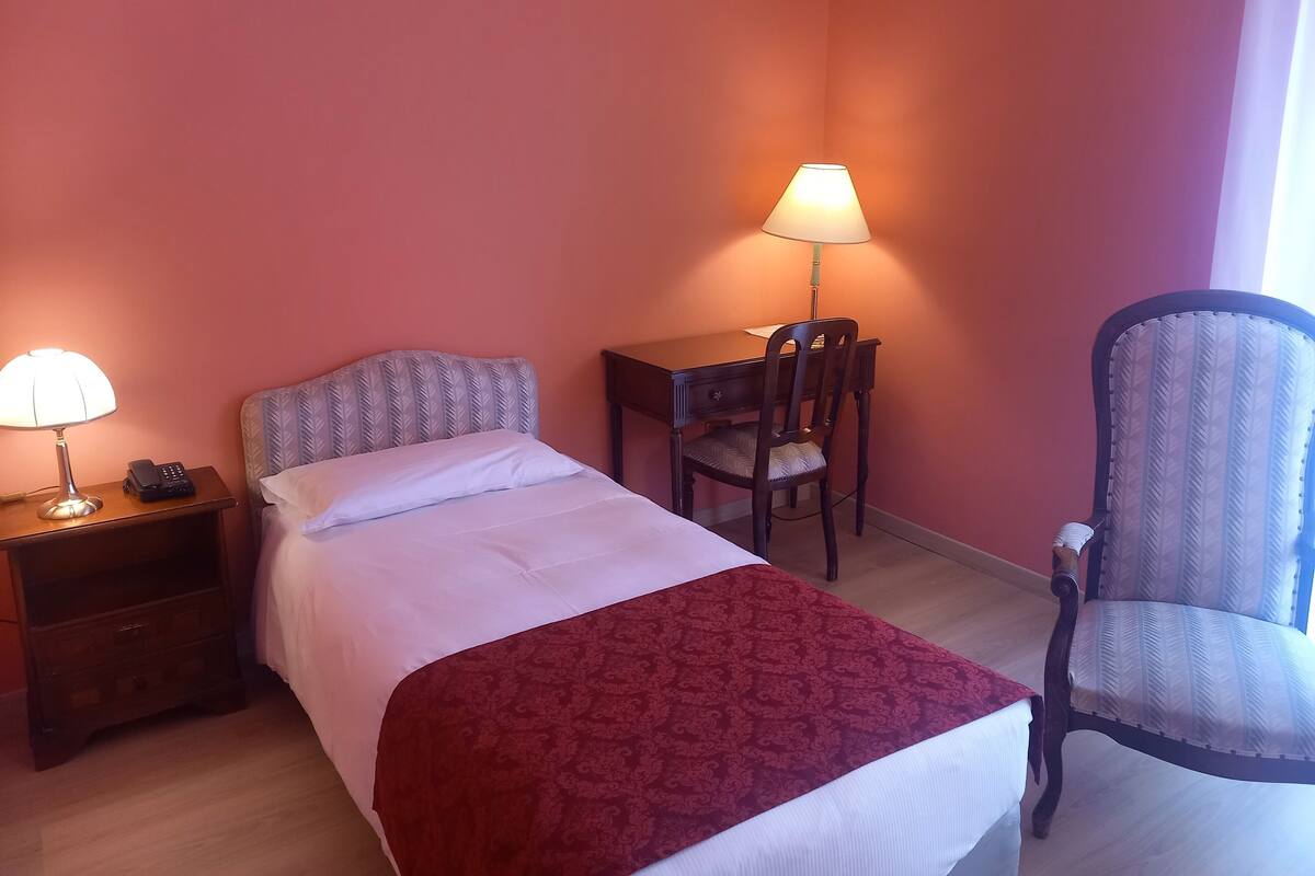 Une chambre d’hôtel comprenant un lit, un bureau, deux chaises, une table de chevet avec une lampe et un téléphone.