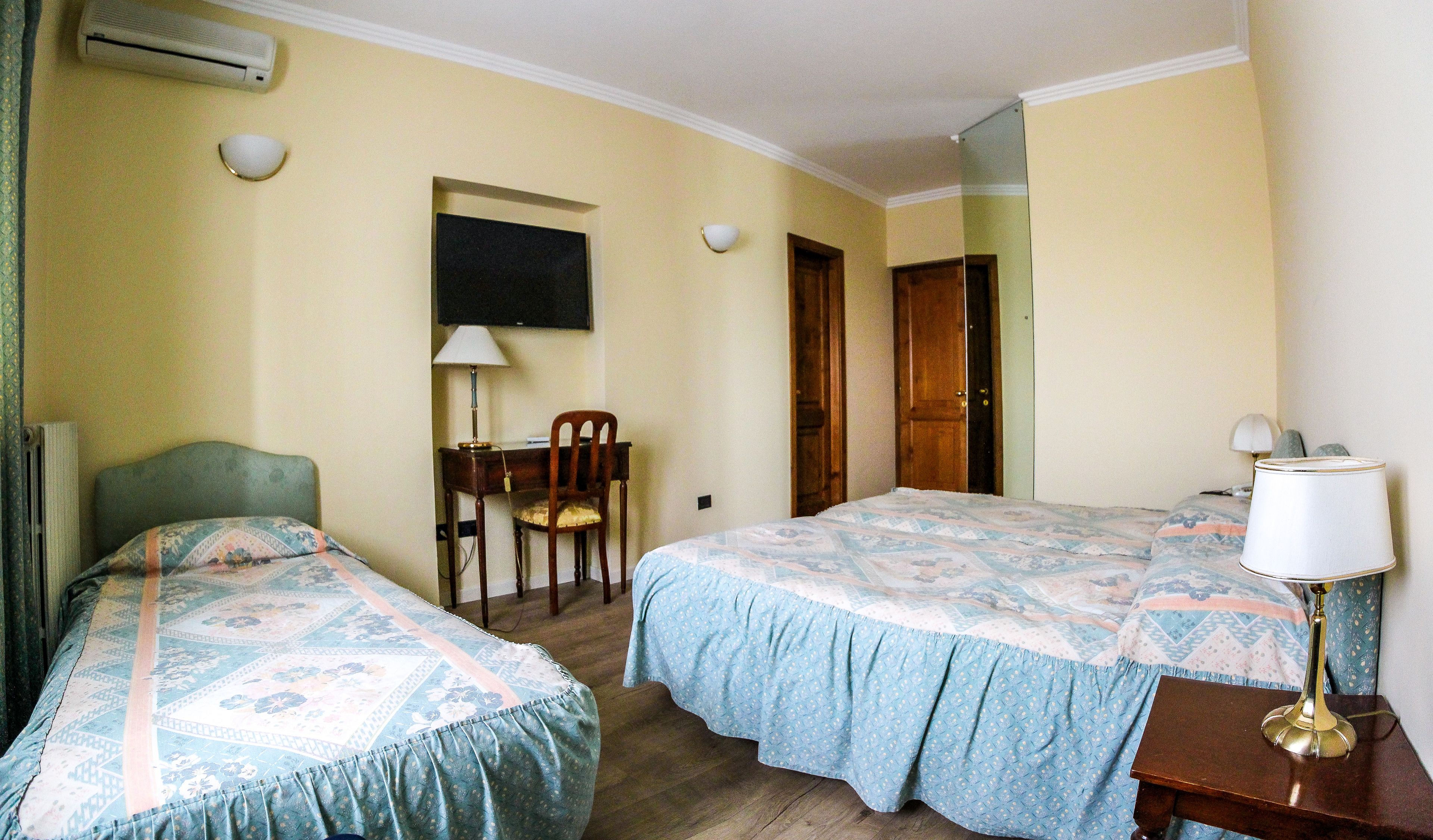 Een hotelkamer met twee enkele bedden, een bureau, een stoel, een lamp en een spiegel.