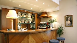Una zona de bar con mostrador de madera, taburetes, una lámpara, una estantería con botellas y un cuadro en la pared.