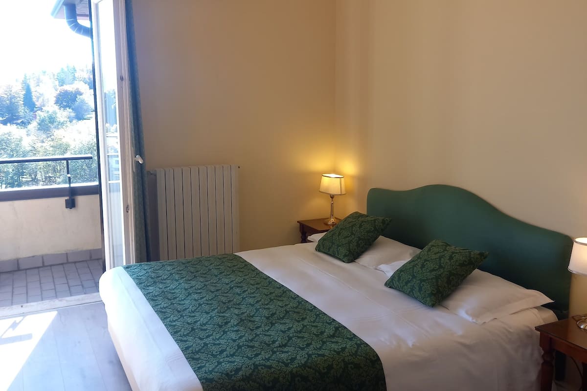 Une chambre d’hôtel comprenant un lit, une table de chevet, une lampe, une fenêtre avec des rideaux et un appareil de climatisation.
