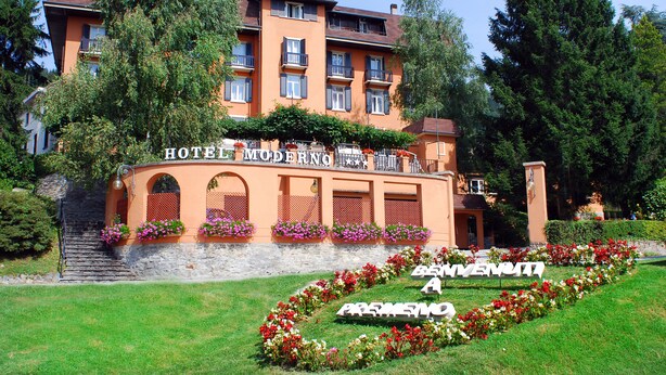 Un hotel con fachada moderna, varios balcones y un jardín bien cuidado con parterres florales.