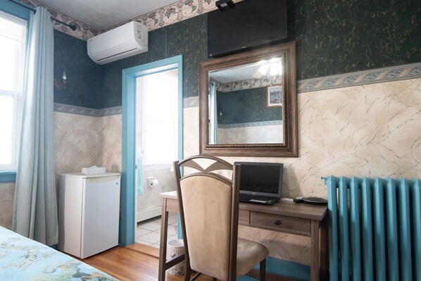 Una habitación con una cama, un escritorio con una computadora portátil, una silla, un radiador y un equipo de aire acondicionado.