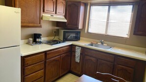 A kitchen with wooden cabinets, a white refrigerator, a microwave, a sink, and a window with blinds.