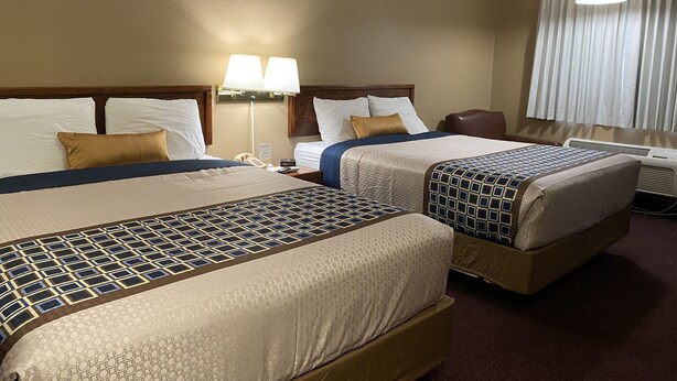 A hotel room with two beds, a desk, a lamp, and a window with curtains.