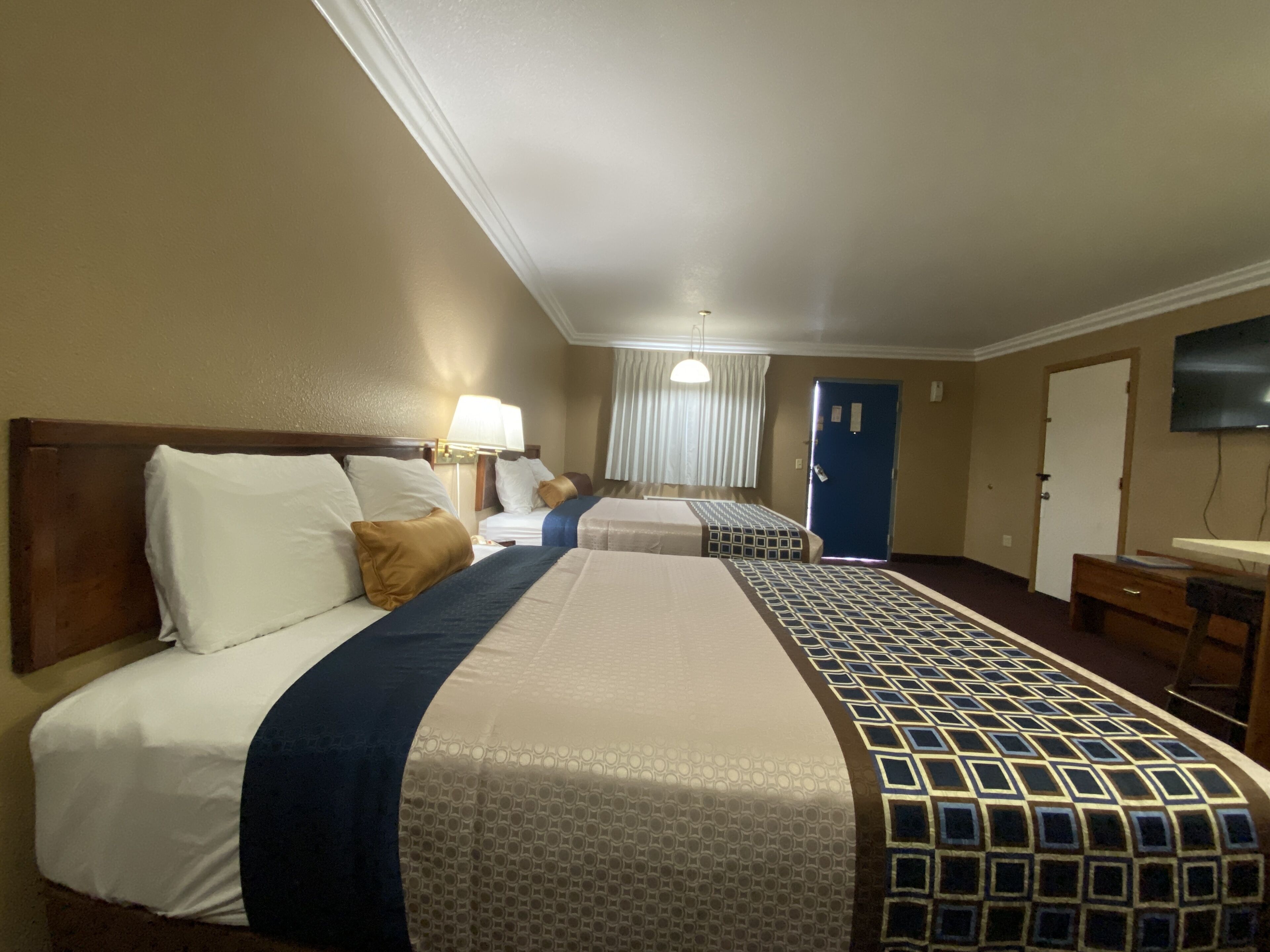 Habitación de hotel con dos camas, televisor, escritorio y ventana con cortinas.