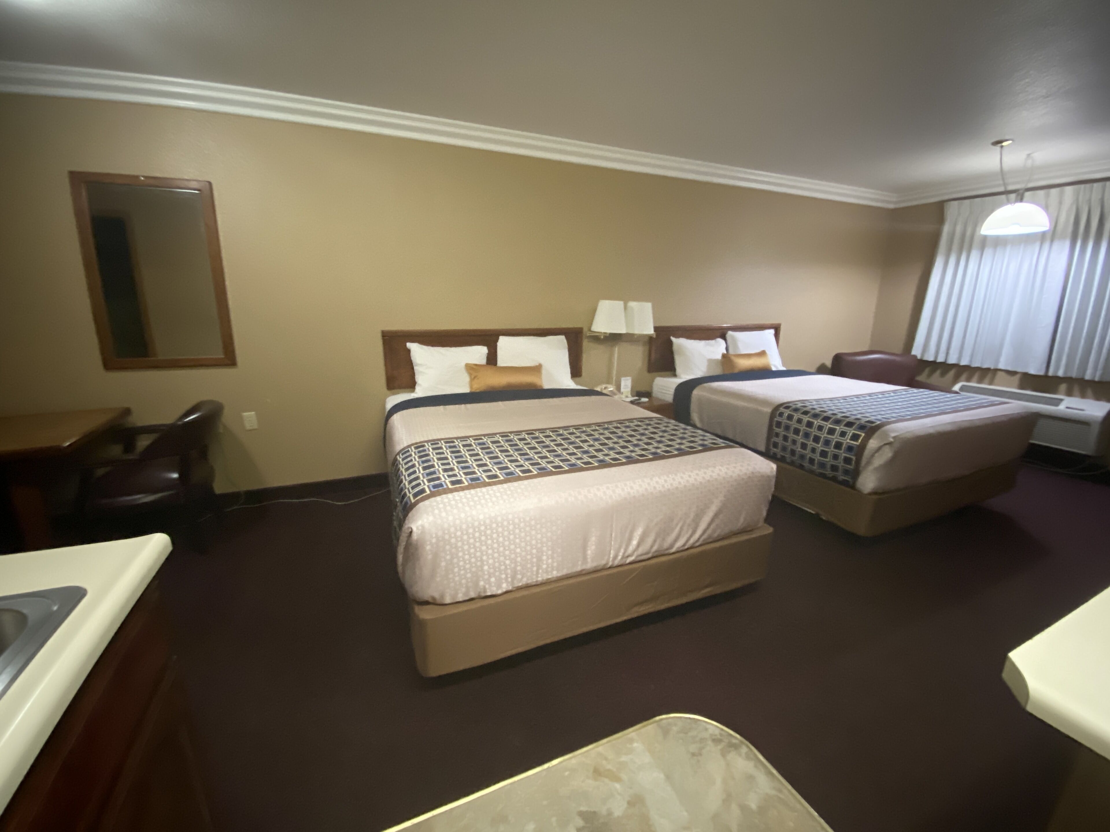 A hotel room with two beds, a desk, a chair, and a mirror.