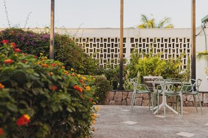 An outdoor patio area with a table and chairs, surrounded by lush greenery and flowering plants.