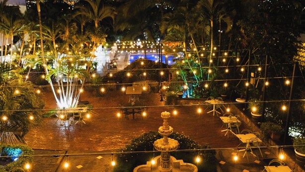An outdoor patio area with string lights, tables, chairs, and a central fountain. - Hotel Honduras Maya (Tegucigalpa)