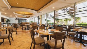 A spacious restaurant with multiple tables and chairs, large windows offering views of greenery, and a modern ceiling design. - Hotel Honduras Maya (Tegucigalpa)